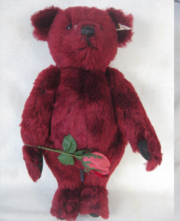 Dark red teddy bear holding a red velvet rose